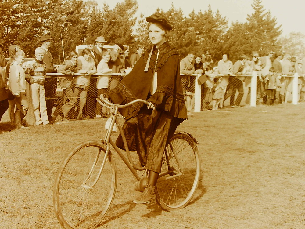 Young girl in period dress cycling in a parade
